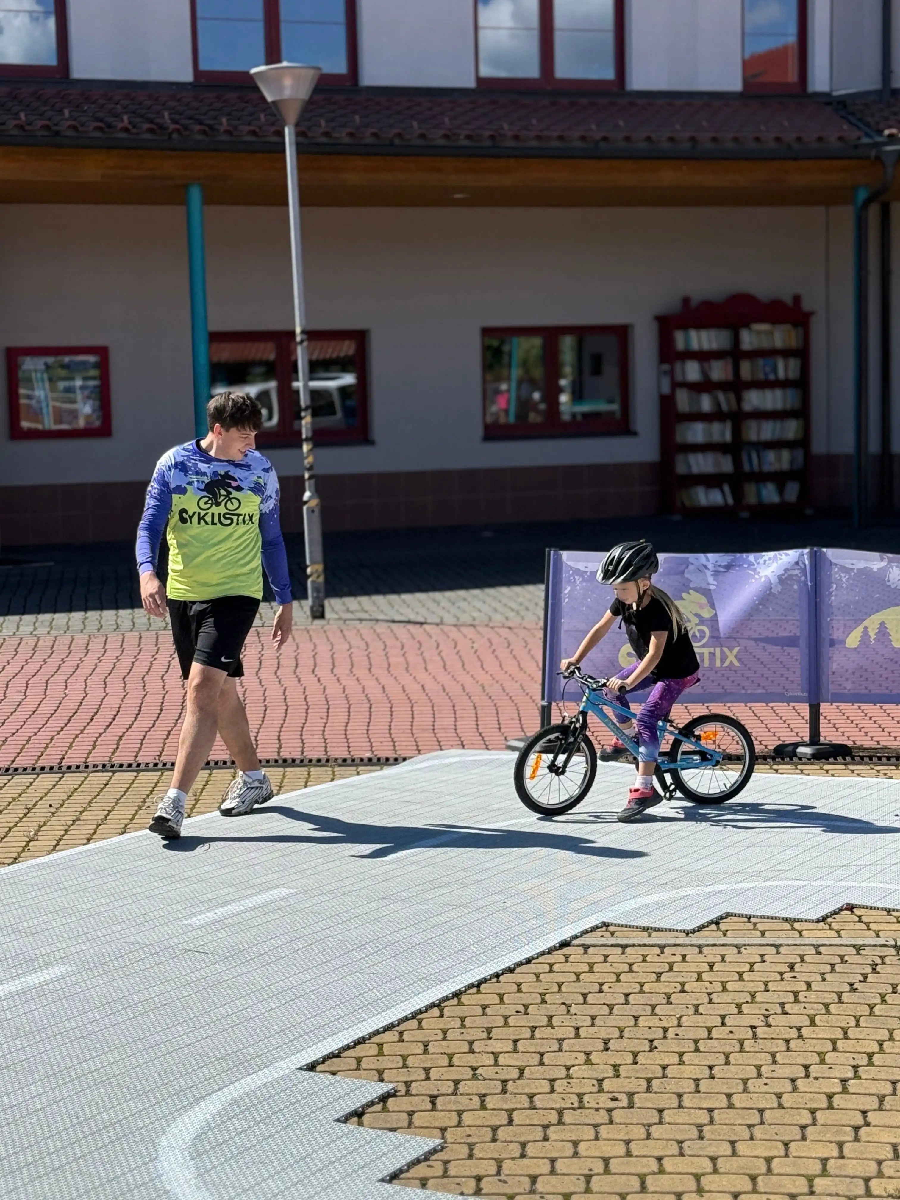 trenér ukazuje cestu dítěti na kole na dětském dopraním hřišti