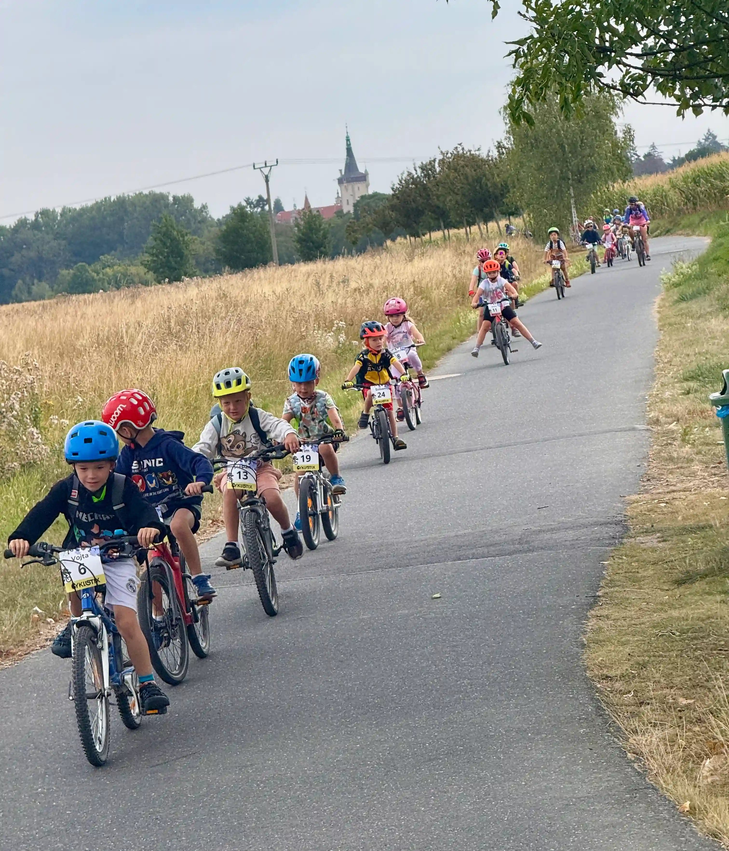 Děti jedou na kolech po cyklostezce v řadě za sebou.