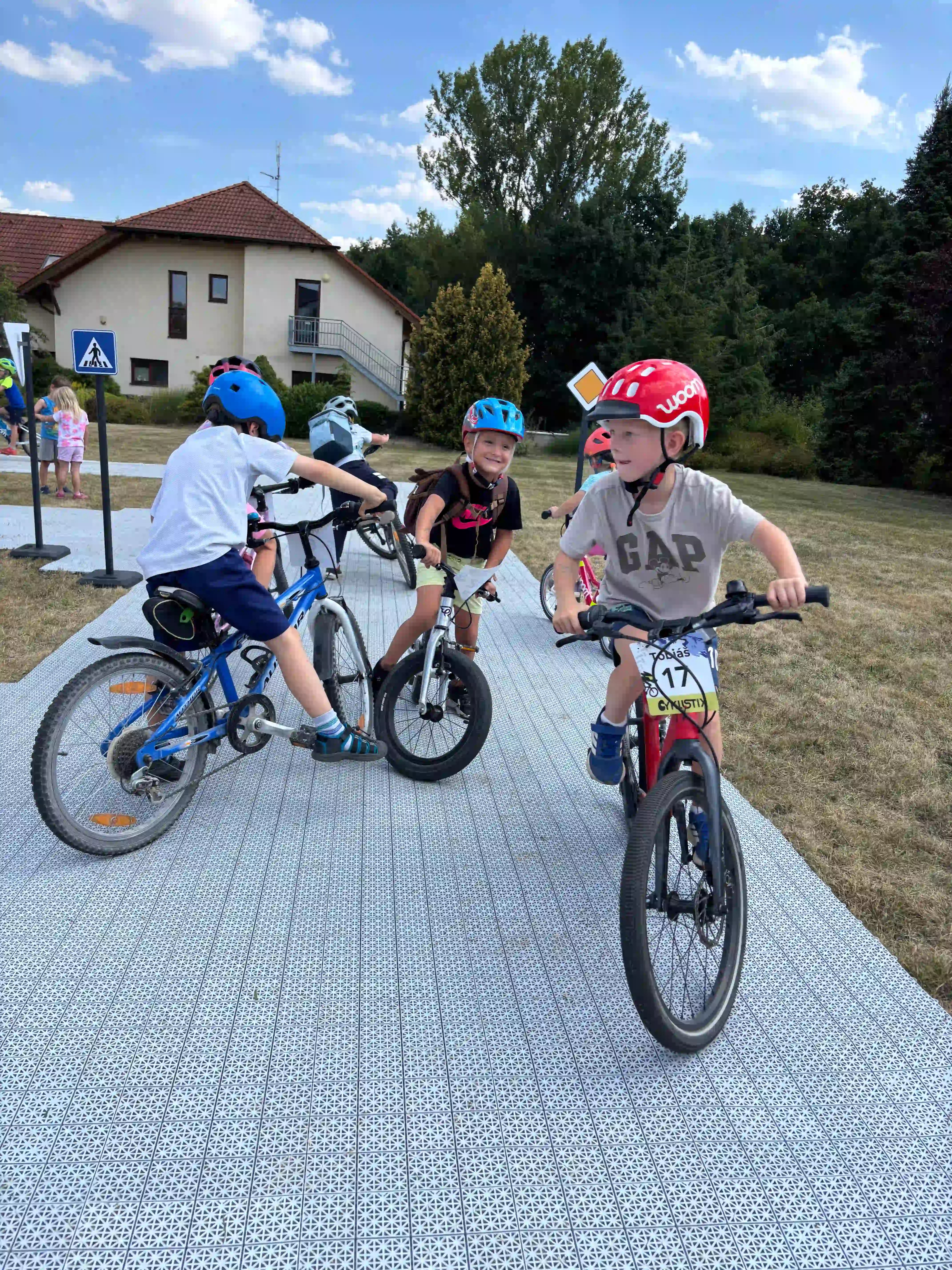 Děti jezdí na kole po dopravním hřišti s dopravními značkami.