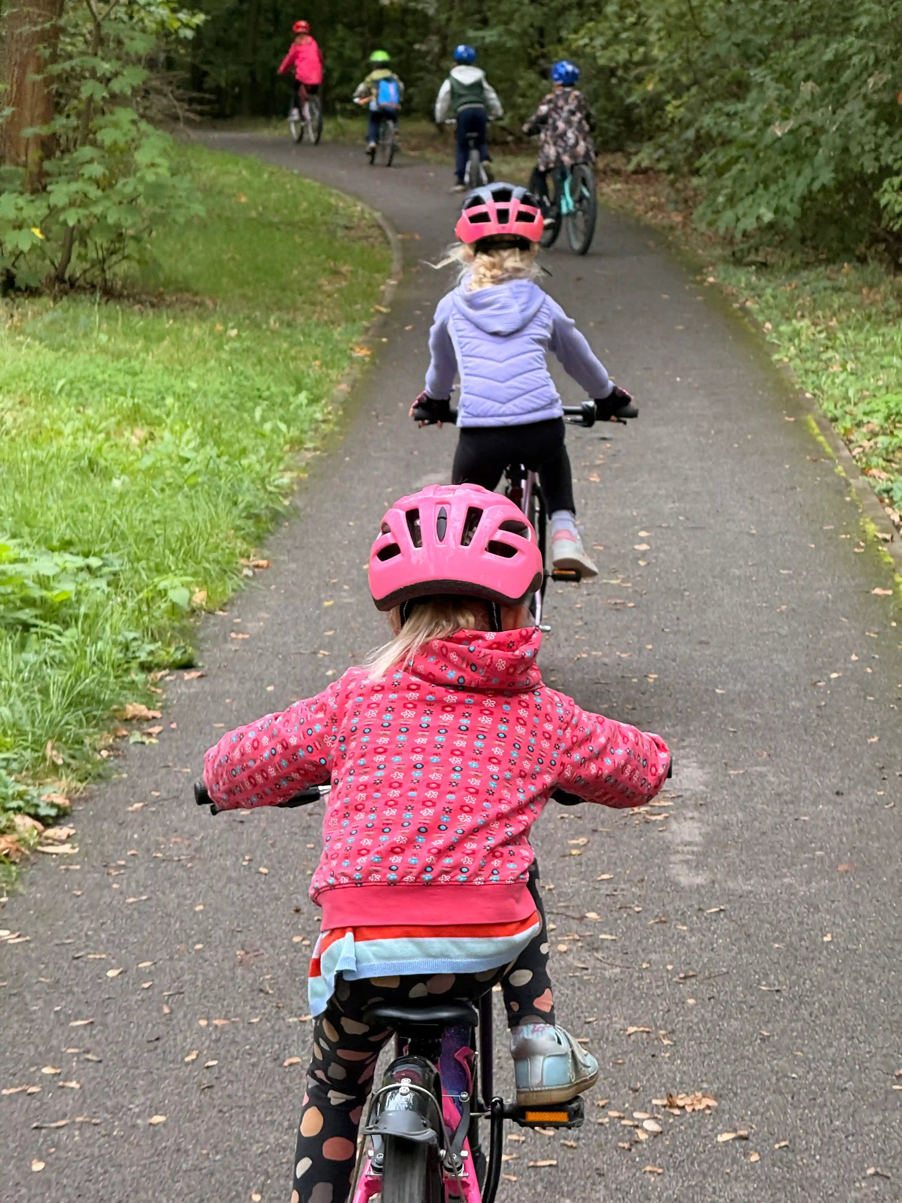 Děti jedou na kolech v řadě za sebou po cyklostezce.