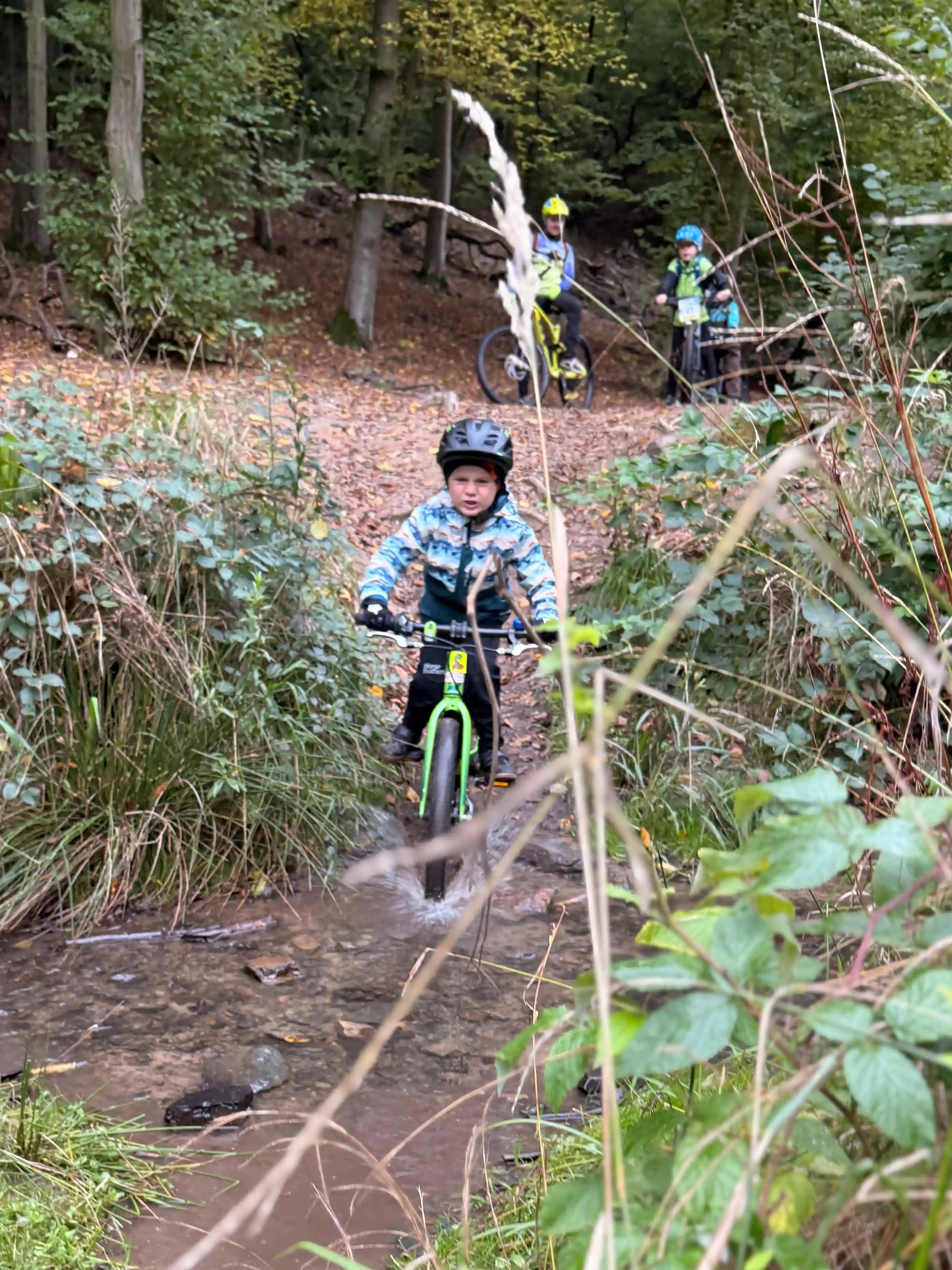 Dítě projíždí potokem na kole a voda stříká všude.