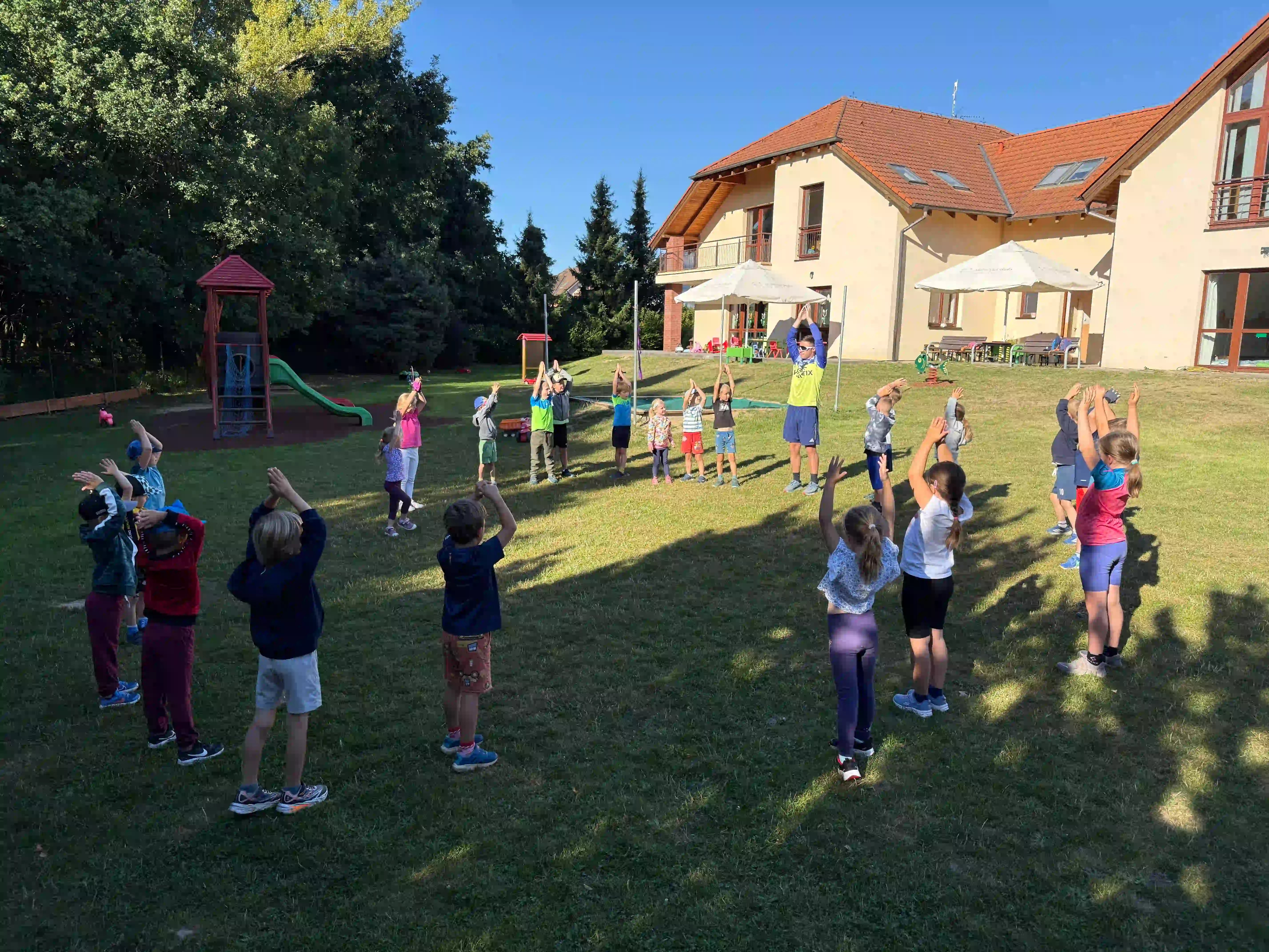 Děti jsou v kroužku a protahují se společně s trenérem.