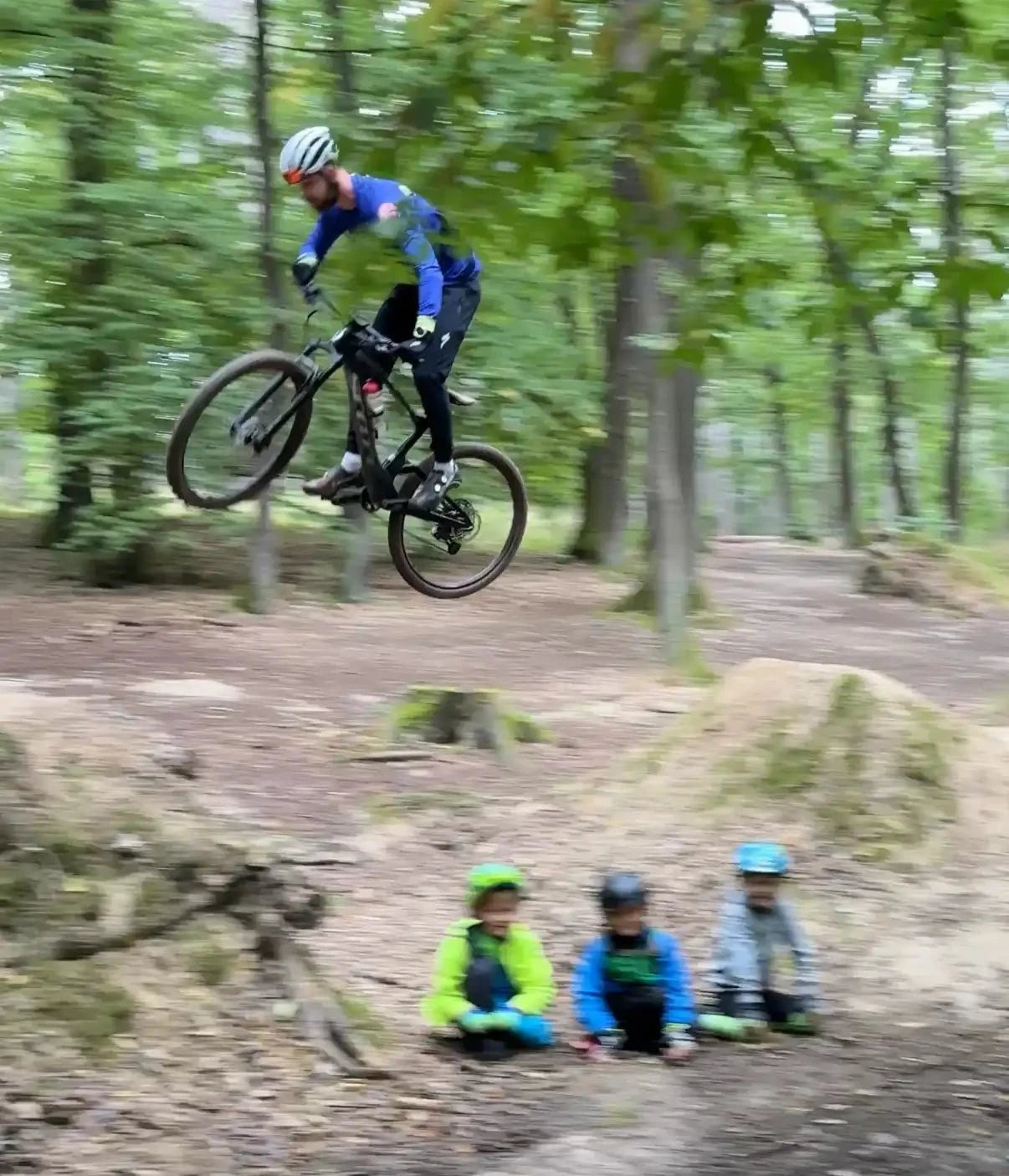 Trenér skáče skok na kole a děti sedí před skokem, vypadá to jakoby je přeskakoval.