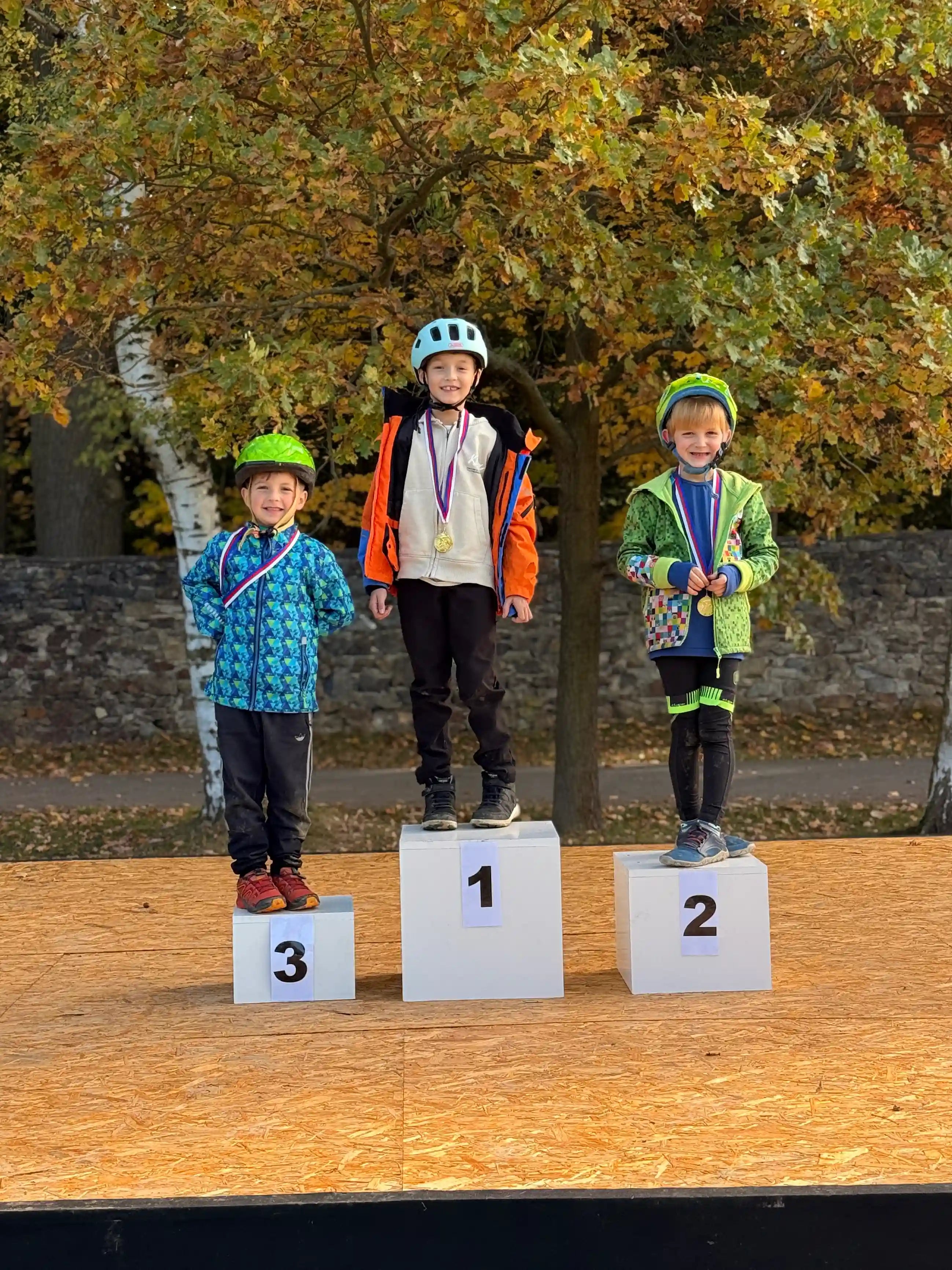 Tři děti stojí na podiu se stupni vítězů a mají medaile.